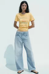 Camiseta color amarillo con efecto lavado, cuello redondo y mangas cortas. Estampado frontal con un oso de los Care Bears™ y la frase "free hugs".