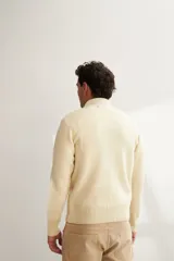 Campera de lana color crema, tejida con cierre delantero, cuello alto y bolsillos delanteros.