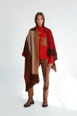 Ruana tejida con diseño geométrico en bloques de color beige, azul y naranja, con flecos en el borde inferior.