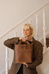 Bolso tipo tote de cuero color marrón, con manijas cortas y correa larga desmontable.