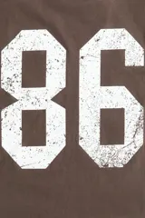 Remera marrón de algodón con corte amplio, cuello redondo y estampado frontal con el número 86 en blanco.