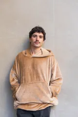 Canguro unisex color beige de tela suave con capucha y bolsillo delantero. Tiene un diseño 2 en 1 que permite usarlo largo o corto ajustando la piola.