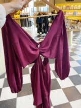 Vestido largo color borgoña, con escote en V, mangas largas abullonadas y falda con volados. Presenta un corte en la cintura con detalle de nudo.