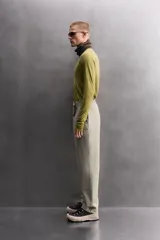 Pantalón de hombre color beige/caqui, de corte regular fit, confeccionado en tejido técnico compacto con elasticidad. Presenta cintura ajustable con cinturón a contraste, bolsillos frontales, bolsillo trasero con cierre de cremallera oculta y bolsillo cargo con cierre de cremallera oculta en la pernera.