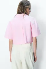 Camisa celeste de popelín con cuello solapa, escote pico y manga corta. Presenta dos bolsillos delanteros de parche y cierre frontal con botones.