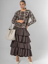 Camisa de tela escocesa liviana, color gris oscuro con líneas en blanco, azul marino y salmón. Presenta un diseño con volados verticales en el frente y mangas abullonadas.