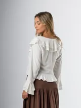Blusa color crudo en lino rayón con volados, de mangas largas acampanadas y cierre frontal con botones.