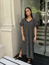 Vestido largo de tejido a rayas horizontales en tonos beige y blanco, con escote en V y mangas cortas tipo murciélago. Presenta tajos laterales en el ruedo.