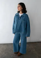 Camisa celeste de denim con cuello clásico, mangas largas con puños abotonados, cierre frontal con botones a presión y dos bolsillos de parche en el pecho.