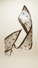 Pañuelo largo y estrecho de seda con estampado abstracto en tonos azules y blancos, con borde blanco y ribete marrón.