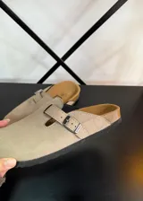 Zuecos beige con hebilla metálica ajustable, plantilla de corcho y suela de goma negra.