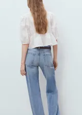 Blusa blanca con bordado floral, cuello de pico, mangas abullonadas tres cuartos y corte peplum.