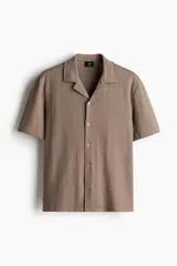 Camisa de manga corta color marrón claro, de punto texturizado de mezcla de algodón, con cuello abierto, tapeta lisa y bajo recto.