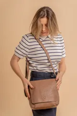 Bandolera de hombro color gris claro, con solapa frontal y correa ajustable. Presenta un diseño simple y práctico, ideal para uso diario.