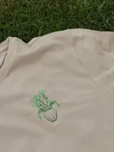 Remera color beige de manga corta con cuello redondo y estampado de un jarrón con flores en color verde.