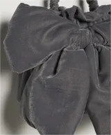 Bolso de terciopelo negro, estilo saco o fruncido, con un gran lazo decorativo en el frente. Posee una correa de hombro ajustable con herrajes dorados.