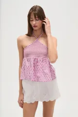 Top sin mangas confeccionado en algodón con estampado integral en tonos rosados. Presenta un diseño con cuello halter cruzado, pechera elástica con técnica de nido de abeja y bajo con volado tipo peplum.