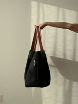 Bolso negro tipo tote de neopreno con bolsillo interno de red, sobre haciendo juego y gancho para sujetarlo.