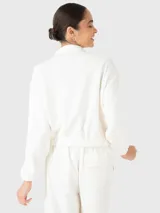 Buzo color blanco de tela suave y ligera con bolsillos en la parte frontal, con cierre y tape con botones para hacerlo invisible; y pretina en la cintura.