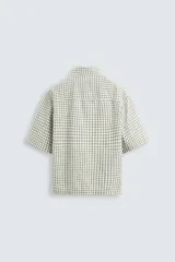 Camisa de hombre de corte boxy fit, confeccionada en tejido de algodón a cuadros en tonos beige, verde y azul. Tiene cuello solapa, manga corta y cierre frontal con botones.