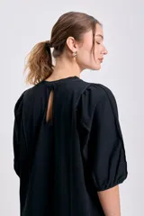 Vestido negro de corte recto y largo midi, con cuello redondo y mangas globo cortas. Presenta pespuntes contrastantes en color claro que recorren el frente y los hombros.