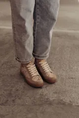 Zapatillas bajas color beige con estampado de piel de serpiente metalizada, cordones blancos y suela color caramelo.