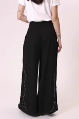 Pantalón palazzo negro con bordado de pequeñas tachas plateadas en forma de rombos a lo largo de la pierna.