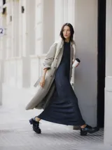 Trench coat largo color beige con doble botonadura, cinturón ajustable y bolsillos laterales.