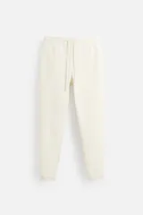 Pantalón jogger color crudo, con cintura elástica ajustable con cordón, bolsillos laterales y traseros de vivo, y bajo con vuelta.