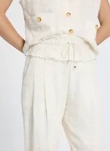 Pantalón jogger color crudo con estampado a cuadros, cintura con cordón ajustable, ribete elástico y minivolantes, bolsillos delanteros, detalles plisados y bajo con botones laterales.