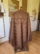 Ruana tejida a mano en color lila, confeccionada en lana merino. Presenta un diseño de punto con calados diagonales y terminación de flecos largos en el ruedo.