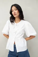 Blusa blanca de algodón con mangas abullonadas, escote redondo y lazos frontales.