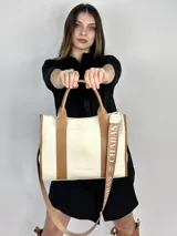 Bolso tote color crema con detalles en cuero marrón. Tiene doble asa de mano y correa de hombro extraíble con el logo de la marca.