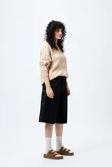 Bermuda carpenter de denim negro, corte relajado y largo a la rodilla, con costuras visibles y múltiples bolsillos funcionales.