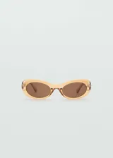 Gafas de sol ovaladas color naranja translúcido con lentes marrones. Fabricadas con residuos reciclados de policarbonato, con protección UV total y filtro de categoría 3.