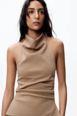 Top color beige de cuello halter y hombros descubiertos, con espalda descubierta, bajo con aberturas laterales y cierre en cuello con botones.