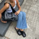 Zuecos negros de cuero encerado con detalle de tachas plateadas en la base y hebilla metálica en el empeine.