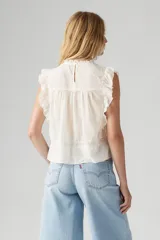 Blusa blanca sin mangas con cuello alto y detalles de encaje y volados.