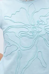 Blusa celeste de lino con bordado en relieve de formas orgánicas y terminaciones desflecadas.