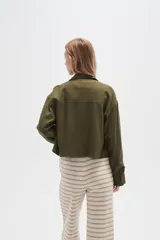 Chaqueta color blanco hueso de lino con cuello camisero, cierre frontal con botones marrones, bolsillos de parche en el pecho y corte holgado.