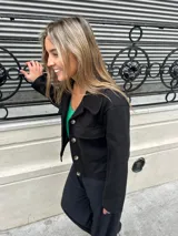 Chaqueta corta negra de lana y viscosa, con cuello clásico, cierre frontal con botones y bolsillos de parche en el pecho.