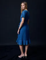 Vestido de tencel azul con escote en V cruzado, cintura elastizada con lazo, manga corta con volados y falda midi con volados.