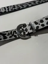 Cinturón con estampado animal print en blanco y negro, con hebilla metálica plateada.