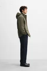 Parka verde militar confeccionada en tejido técnico ligero resistente al viento, con cuello alto, capucha, manga larga con puños ajustables, bolsillos de plastrón con solapa en la cadera, bolsillo interior, bajo ajustable con elásticos y cierre frontal con cremallera oculta por solapa con botones a presión.