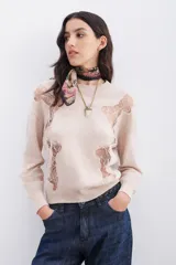Sweater color crudo de tejido liviano con cuello redondo y calce holgado. Presenta ajustes en los puños y el ruedo con terminaciones en punto rib, y una badana con el logo de la marca en la espalda. Los recortes en encaje de formato irregular aportan transparencias.