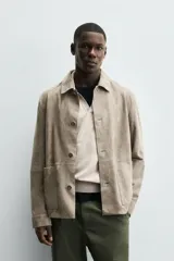 Cazadora de hombre de corte regular fit, confeccionada en piel con acabado ante color beige claro. Presenta cuello solapa, manga larga con puño de botón, bolsillos de plastrón en la cadera y cierre frontal con botonadura.