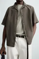 Camisa color marrón oscuro de corte relaxed fit, confeccionada en tejido de lino. Tiene cuello bowling, manga corta, bajo con aberturas laterales y cierre frontal de botonadura.