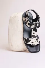 Sandalias planas con tiras de cuero con estampado de vaca en blanco y negro, y hebilla lateral.
