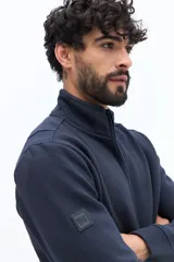 Campera de algodón con cierre frontal, cuello alto en color verde oliva y cuerpo texturado con patrón de espiga en tono marrón topo. Las mangas son lisas y del mismo tono que el cuerpo. Presenta un pequeño logo bordado en el pecho.