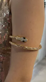 Brazalete rígido dorado con forma de serpiente. La cabeza de la serpiente está cubierta de strass y tiene ojos negros.